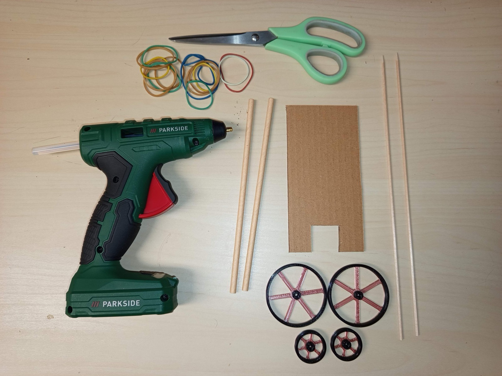 Materiál na autíčko: kartonový podvozek s výřezem, špejle, čtyři kola, gumičky, nůžky a tavná pistole